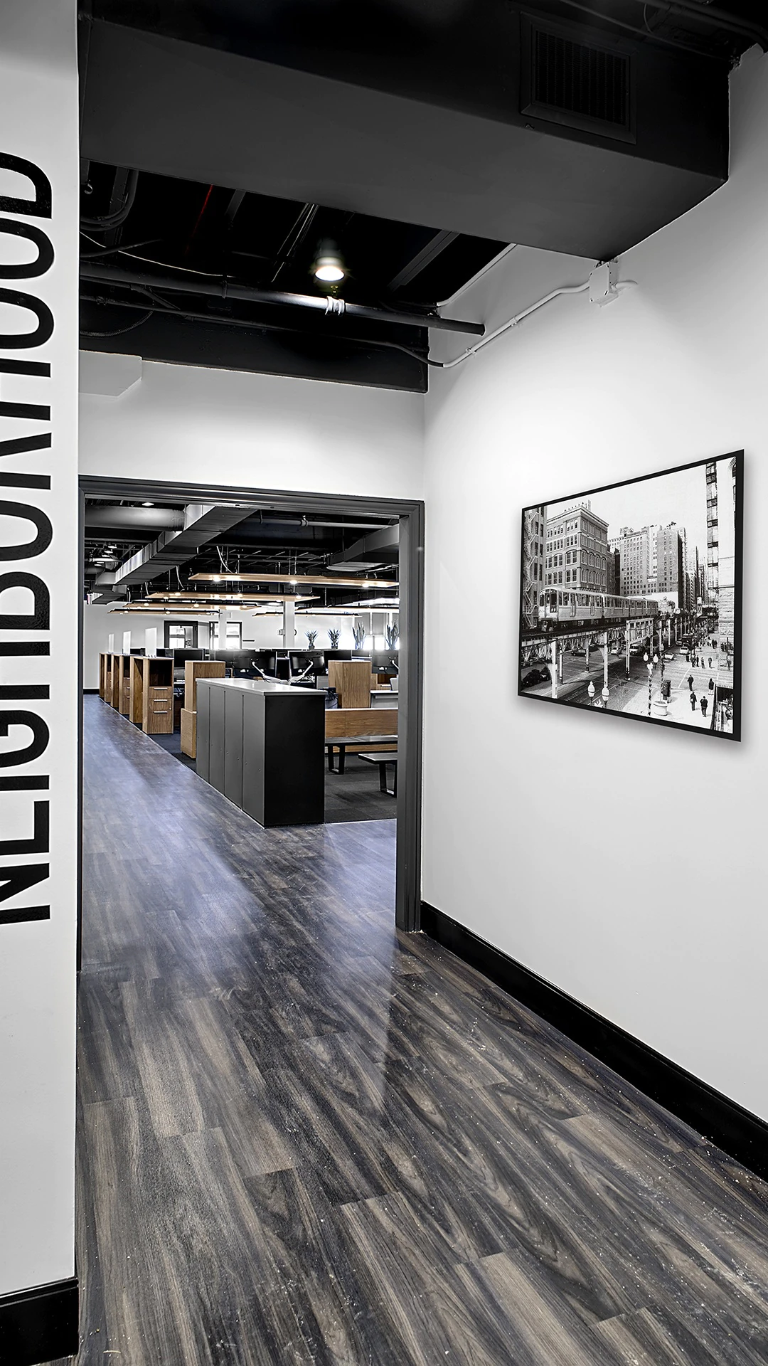 Office Interior Black-and-white office hallway leading to an open workspace with cubicles; framed cityscape photo on the wall.