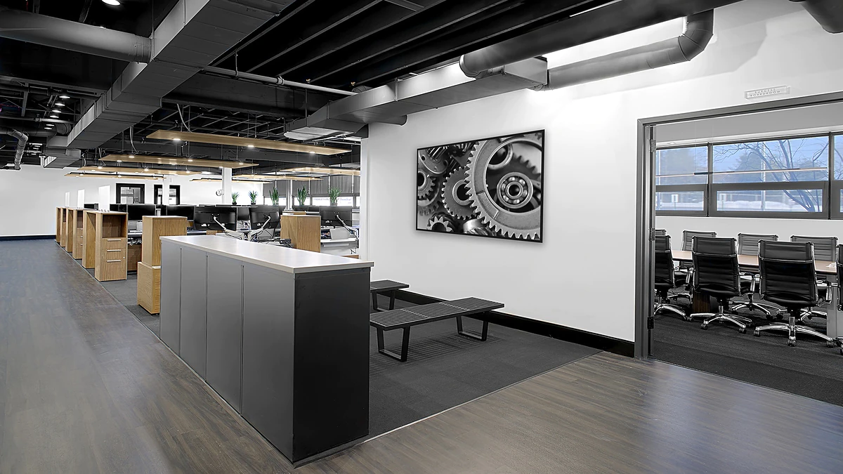 Office Interior Open-plan office with exposed ceilings, row of cubicles, a front counter, wall-mounted gear art, and a conference room.