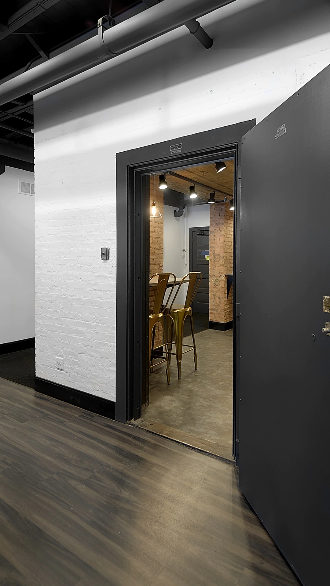 Office Interior Industrial doorway opens to brick interior with gold metal bar stools under warm pendant lighting.