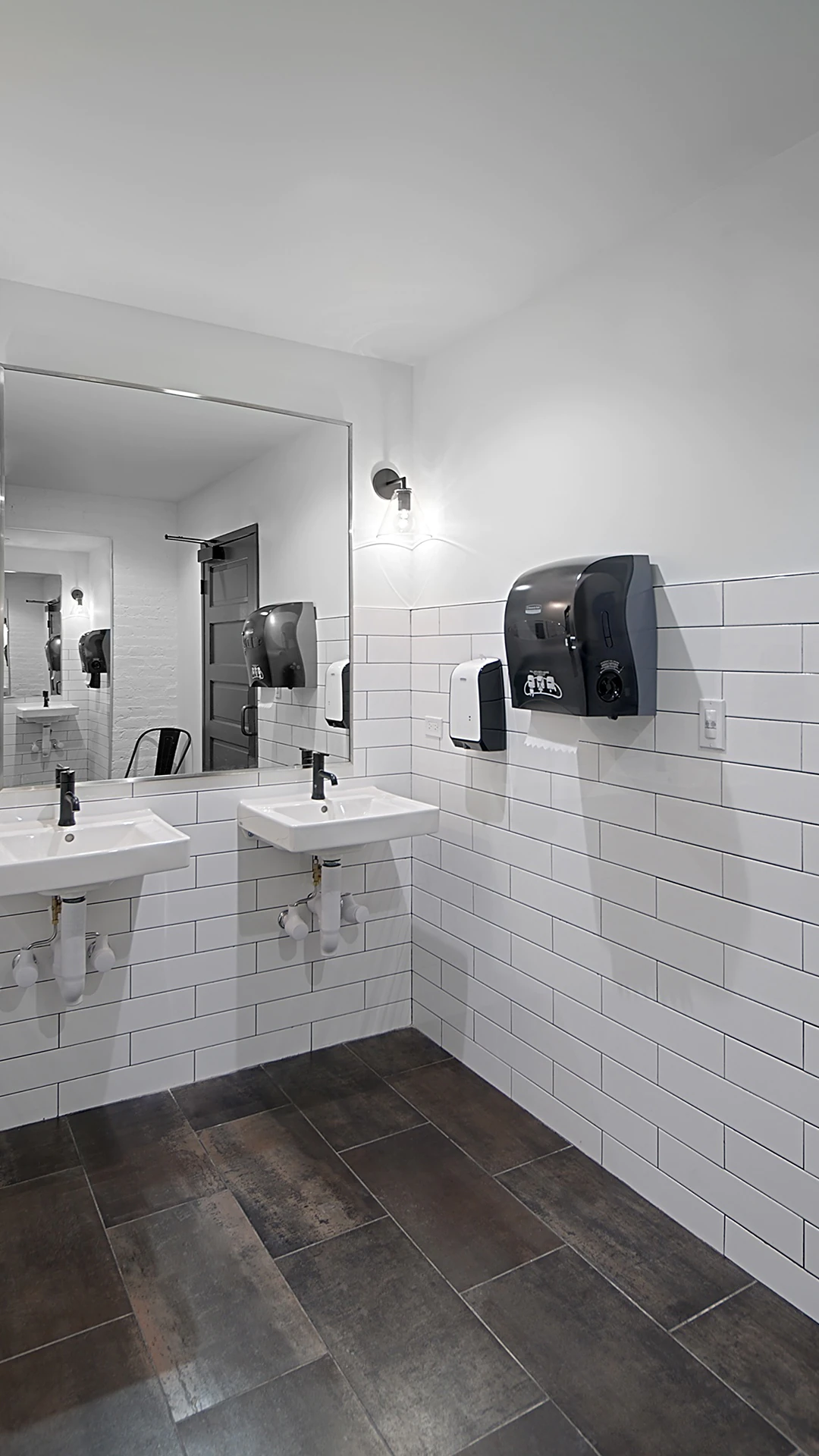 Office Interior Gray-scale public restroom with two white sinks, large mirror, tiled walls, and soap and paper-towel dispensers.