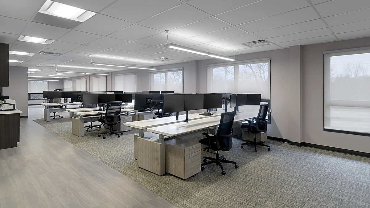 Office Interior Open-plan office with rows of desks, dual monitors, ergonomic chairs, and large windows letting in natural light.