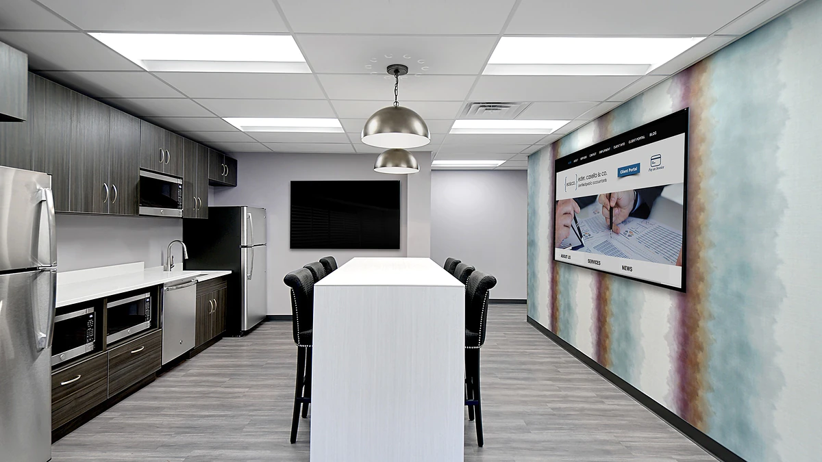 Office Interior Modern office kitchenette with stainless appliances, a long white table and black chairs, large screen on mural wall.