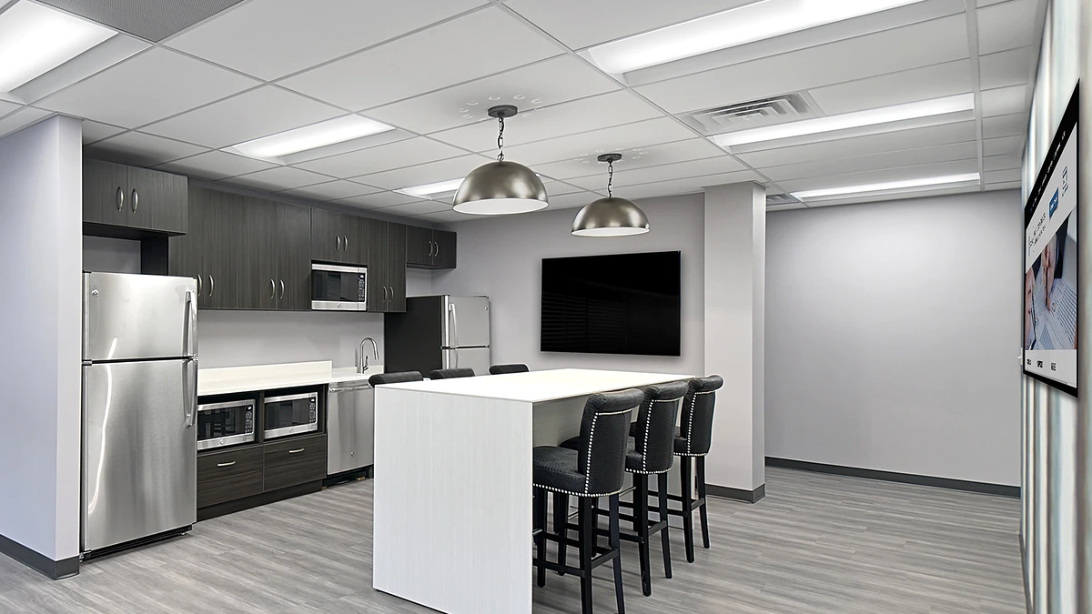 Office Interior Modern office kitchenette with stainless steel fridge and appliances, white island and bar stools under pendant lights.