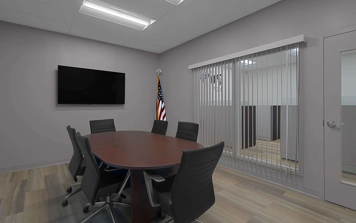 Office Interior Modern conference room with a dark wood oval table, black chairs, a wall-mounted TV, an American flag, and vertical blinds.