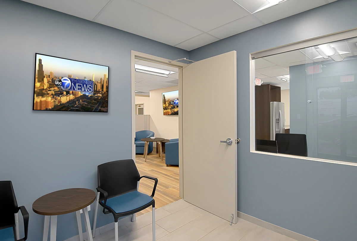 Office Interior Office waiting area with blue walls, wall-mounted ABC7 Eyewitness News screen, open door to lounge with seating.
