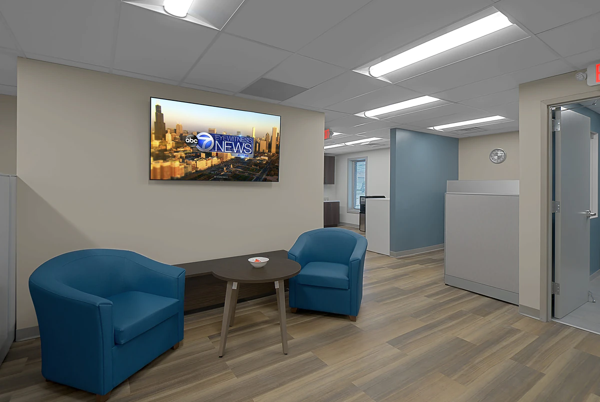Office Interior Modern office lounge with two blue armchairs, a round table, and a wall-mounted TV showing ABC7 Eyewitness News.