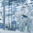Development Factory Cleanroom: Engineers Wearing Coveralls and Goggles while Talking and Using Tablet Computer. Scientists Working in Advanced Electronics Manufacture with Precision Machinery